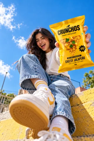 Woman in denim holding a bright yellow Crunchos Cheesy Jalapeno snack bag outdoors in natural sunlight.